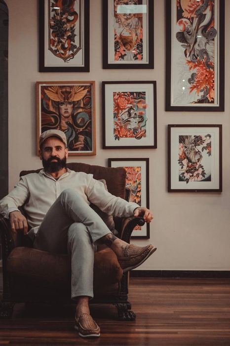 Denis Vazios sentado no studio, diante das suas obras